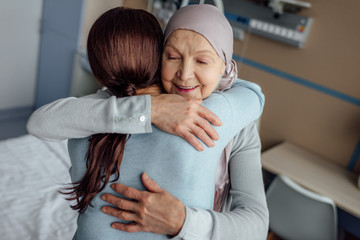 smiling senior woman in kerchief hugging daughter in hospital