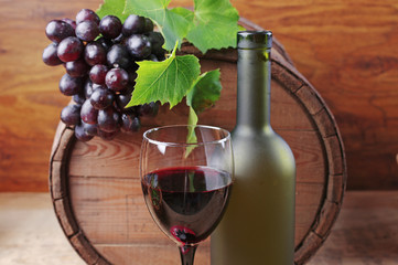 A glass of red wine, a bottle, and a grapes on the background of a wine barrel.