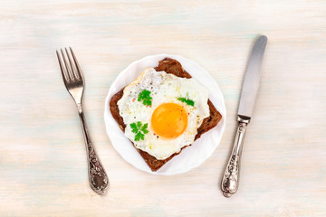 An egg cooked sunny side up on a toast, shot from above with a fork, knife and a place for text