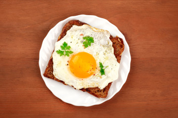An egg cooked sunny side up on a toast, shot from the top on a rustic wooden background with copy space