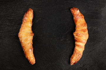 Two croissants on a black background, shot from above, forming brackets for copy space