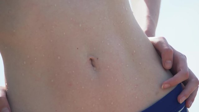 The slender brunette in bikini on the beach, her tanned body of water drops. Morning summer vacation on the coast.