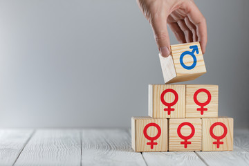 Hand putting a wooden cube with male icon on top of cubes with female logos