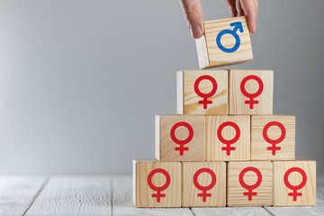 Hand putting a wooden cube with male icon on top of cubes with female logos