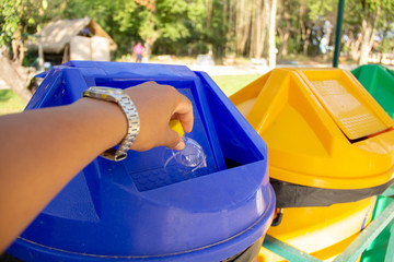Man's hand throwing plastic water bottle in blue bin.
