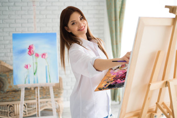 Сute girl artist paints on canvas painting on the easel. Model in the studio