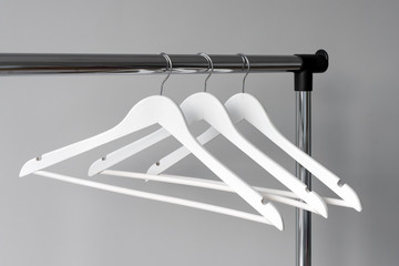 Empty clothes hangers on metal rail against grey background. Rectangular metal clothing rail with...