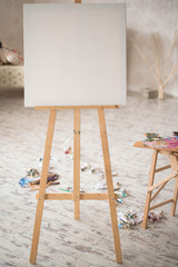 Artistic equipment: easel, paint brushes, tubes of paint, palette and paintings on work table in a artist studio.