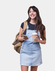 Young beautiful woman with smart phone and cup of coffee isolated on gray background. Cute student girl portrait 