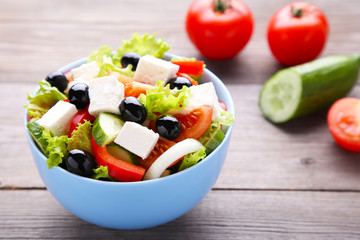 Fresh greek salad on bowl with vegetables on grey wooden background