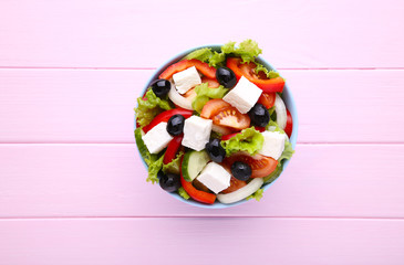 Fresh greek salad on bowl on pink wooden background