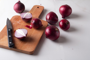 red onions on a cutting board on a white marble background.