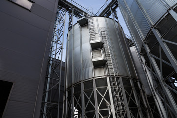 Obraz premium Exterior of Agricultural Silo building with storage tanks for agricultural crops processing plant, drying of grains, rape, wheat, corn, soy, sunflower.
