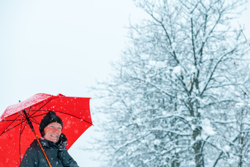 Smiling woman talking on mobile phone under umbrella in snow