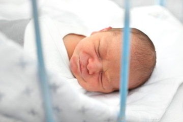 Nowonarodzone dziecko w szpitalu. Pierwsze dni na świecie, noworodek śpi w łóżeczku. - obrazy, fototapety, plakaty