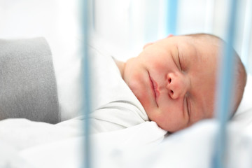 Śpiący noworodek. Pierwsze dni na świecie, noworodek śpi w łóżeczku. - obrazy, fototapety, plakaty