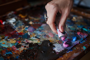 The artist woman squeezes the paint from the tube on the artistic palette. No face. Selective focus.