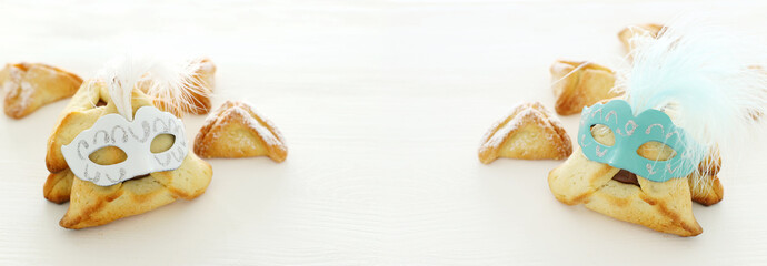 Purim celebration concept (jewish carnival holiday). Traditional hamantaschen cookies with cute mask over white wooden table.