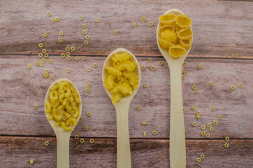 Dried pasta food selection in wooden spoons over old oak background.