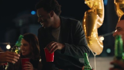 group of multiracial friends celebrating birthday party on rooftop at night drinking alcohol making toast to friendship having fun sharing celebration