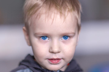 Close up portrait of cute caucasian baby boy with very serious face expression. Bright blue eyes, fair hair. Strong emotions. Indoors, copy space.