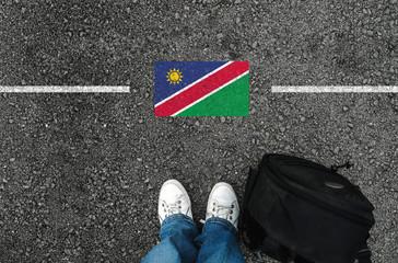  a man with a shoes and backpack is standing on asphalt next to flag of Namibia and border