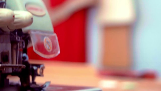 a seamstress working with sewing machine and trim off the excess thread with scissors. close-up of hand work