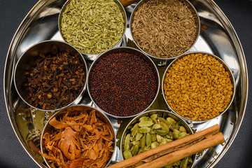 Spices such as chili, cinnamon, cardamom, cumin, fennel seeds and clove on kitchen table and containers. 