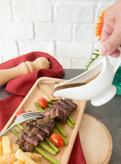 dry aged sliced roast beef with vegetable grilled ,mushroom asparagus tomato french fries and gravy souce on wooden plate