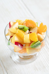 Naklejka na ściany i meble Close-up glass bowl with fruit salad on white wooden table.