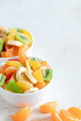 Fototapeta na wymiar Two white bowls with fruit salad and mandarin slices on white background.