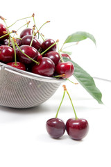 Steel colander with red sweet cherry isolated on a white background..