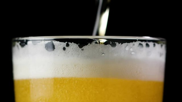 4K Slow motion beer pouring into the glass with foam bubble against dark background