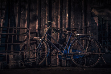 Fototapeta na wymiar old cycle tied with chain, bicycle standing at dark, old bicycle in blue color