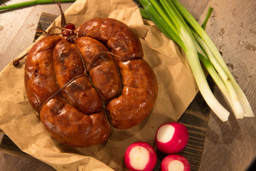 Homemade chicken sausage tied with a rope lies on a wooden board with vegetables