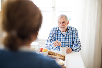 A senior couple sitting at the table at home, having breakfast.