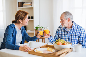 A senior couple sitting at the table at home, having breakfast.