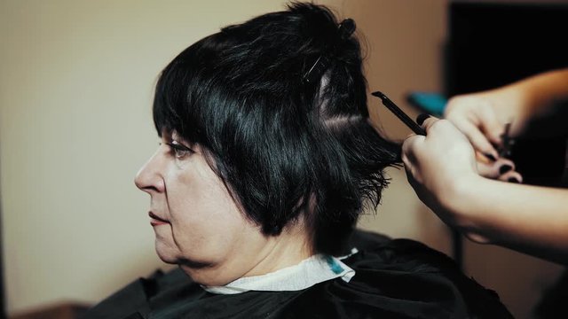 Mature Woman Having Her Hair Cut At The Hairdresser's. Closeup View Of A Hairdresser's Hands Cutting Hair With Scissors, Side View.