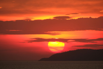 Impressive sunset over the sea and forest island with dramatic orange red fiery sky and dark clouds