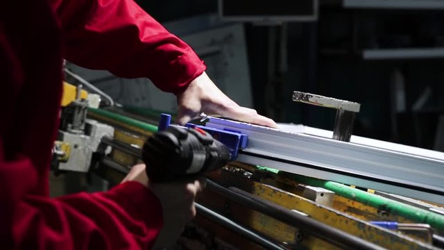 Manufacture of plastic windows and doors. Worker fastens the fittings with a screwdriver to the plastic window in the shop for the production of plastic and metal windows and doors. Screwing screws.
