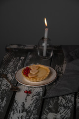 a dessert of lemon tartlet decorated with pastry hearts and pomegranate seeds, rustic style, candle light is on the background 