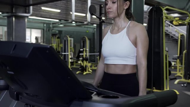Beautiful Young Woman Athlete Walks On A Treadmill Ending An Exercise Session In The Gym. Healthy Lifestyle Concept