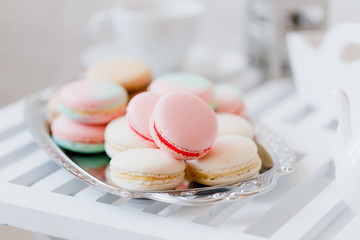 Fototapeta premium Colorful pastel pink, blue, yellow and beige french macaroons on steel tray on white wooden table. Macarons close up.