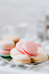 Colorful pastel pink, blue, yellow and beige french macaroons on steel tray on white wooden table. Macarons close up.
