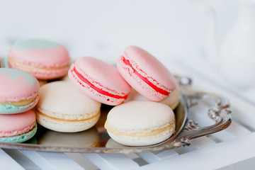 Colorful pastel pink, blue, yellow and beige french macaroons on steel tray on white wooden table. Macarons close up.