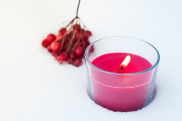 a red candle stands in the snow. On the background of the candle is a branch of the guelder rose