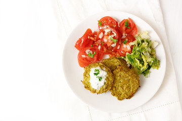 broccoli pancakes with yoghurt dip, lettuce and tomato, healthy slimming food, white plate on a white table with copy space, high angle view from above