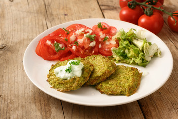 vegetable broccoli pancakes with yoghurt dip, lettuce and tomato, healthy slimming food, white plate on a rustic wooden table