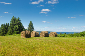 Beautiful summer landscape with sloping meadow, hay, forest and river with blue sky with clouds.