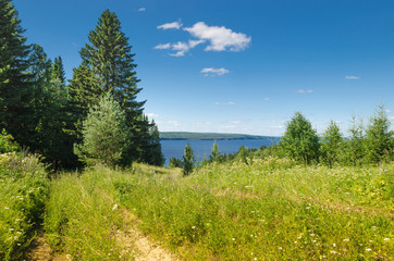 Beautiful summer landscape with sloping meadow, hay, forest and river with blue sky with clouds.